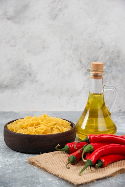 Bol en bois de pâtes crues aux piments rouges et huile sur marbre.