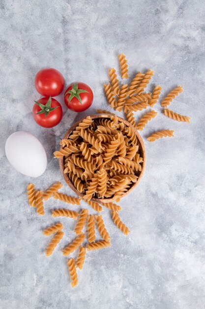 Un bol en bois de pâtes sèches italiennes non cuites Fusilli rigate aux tomates. Photo de haute qualité