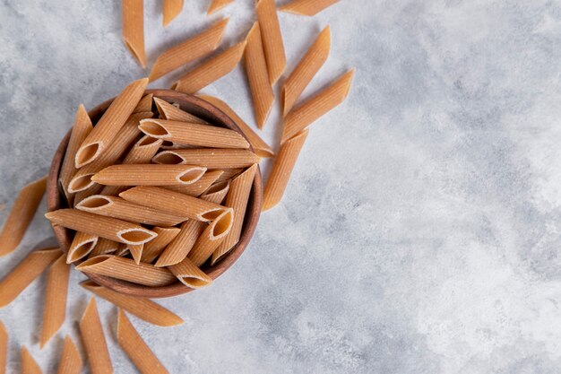 Un bol en bois de pâtes sèches italiennes non cuites Penne rigate. Photo de haute qualité