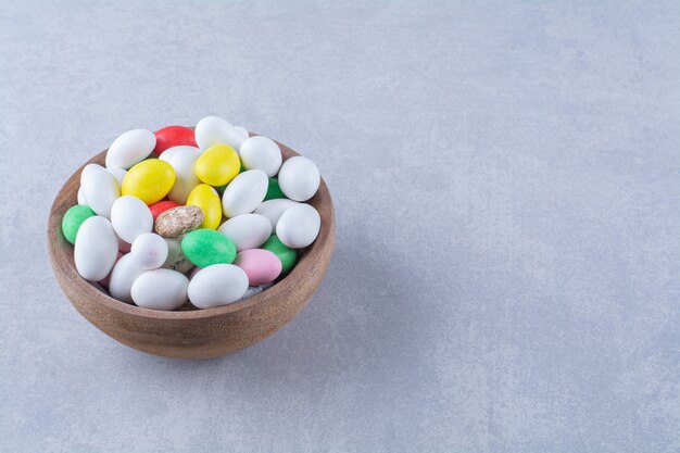 Un bol en bois plein de bonbons aux haricots colorés sur fond gris. photo de haute qualité