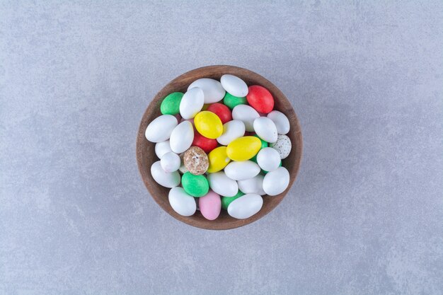 Un bol en bois plein de bonbons aux haricots colorés sur fond gris. photo de haute qualité