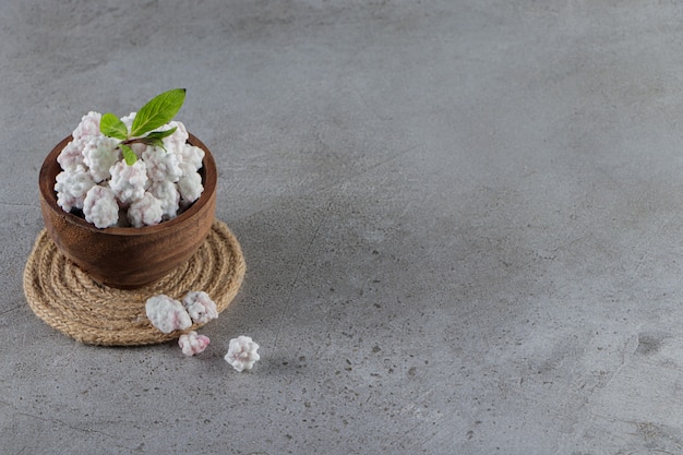 Un bol en bois plein de bonbons blancs sucrés avec des feuilles de menthe sur une pierre