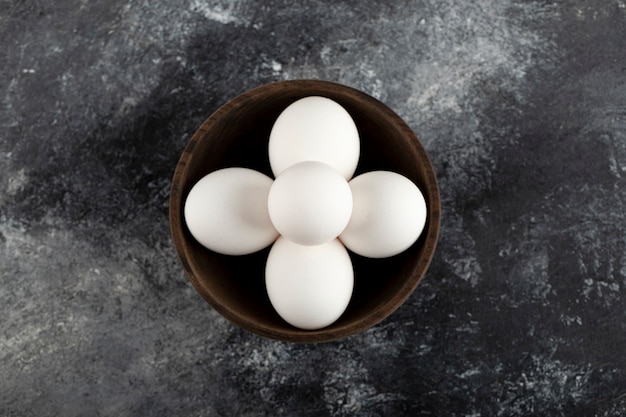 Un bol en bois plein d'oeufs de poule crus blancs.