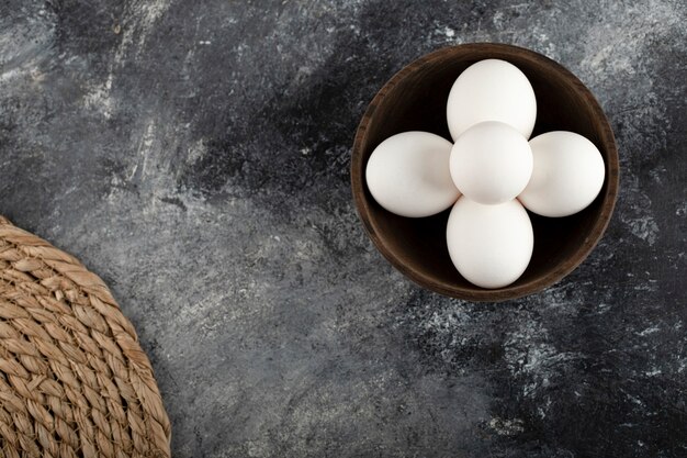 Un bol en bois plein d'oeufs de poule crus blancs.