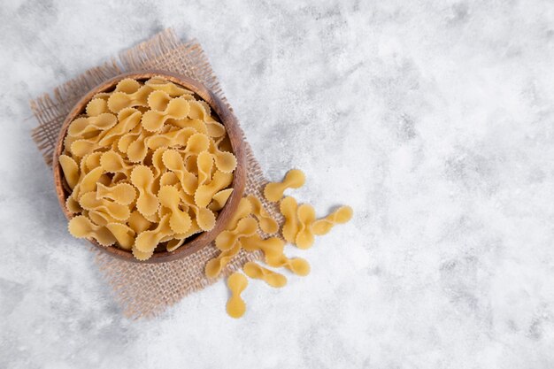 Bol en bois plein de pâtes Farfalle sèches crues posées sur une table en marbre. Photo de haute qualité