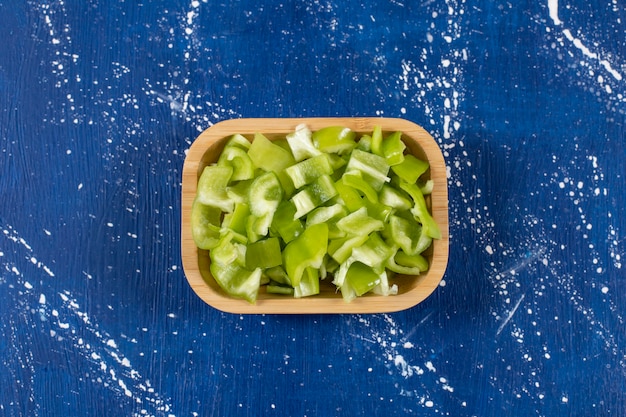 Photo gratuite bol en bois de poivrons verts tranchés sur une surface en marbre.