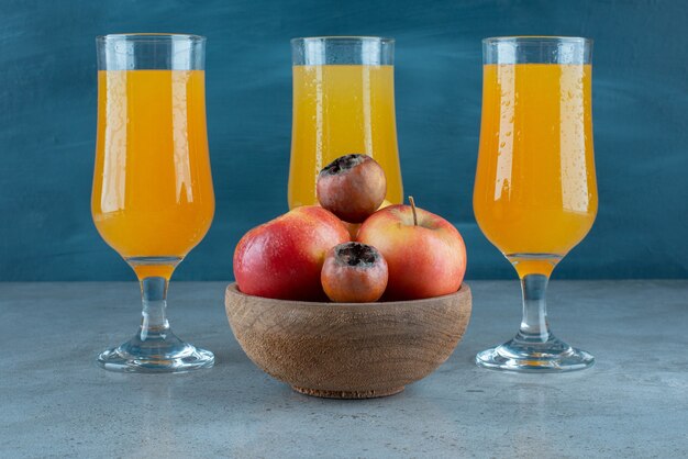 Un bol en bois de pommes avec des tasses en verre de jus d'orange.