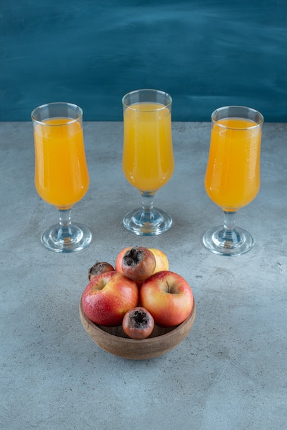 Un bol en bois de pommes avec des tasses en verre de jus d'orange.