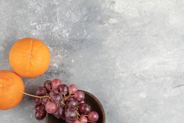 Bol en bois de raisins rouges frais et d'oranges sur une surface en marbre.