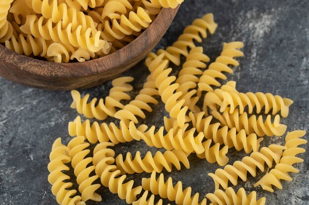 Un bol en bois rempli de pâtes fusilli crues et sèches.