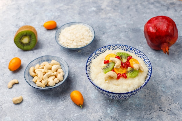 Bol de bouillie de flocons de riz avec des tranches de kiwi, des graines de grenade, des cumquats et des noix de cajou, vue de dessus