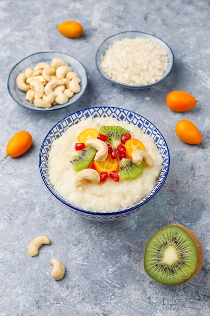 Bol de bouillie de flocons de riz avec des tranches de kiwi, des graines de grenade, des cumquats et des noix de cajou, vue de dessus