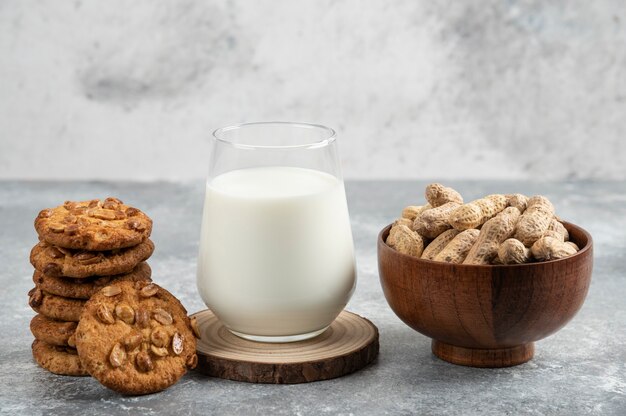 Bol de cacahuètes, verre de lait et biscuits aux cacahuètes biologiques sur table en marbre.