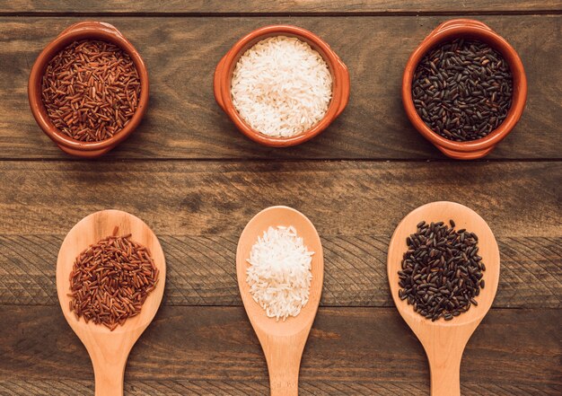 Bol et cuillère en bois avec du blanc; grains de riz rouges et noirs sur table en bois