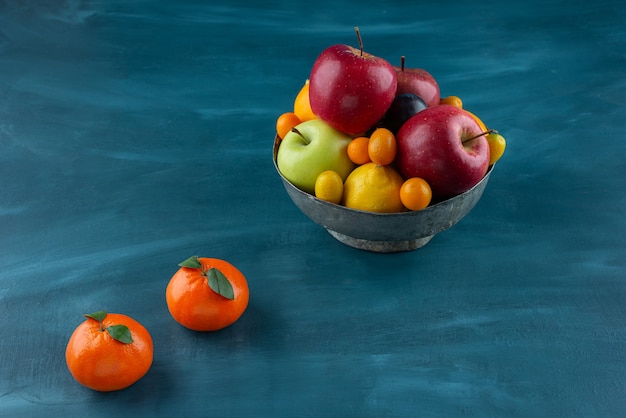 Bol de divers fruits frais placés sur une surface bleue.