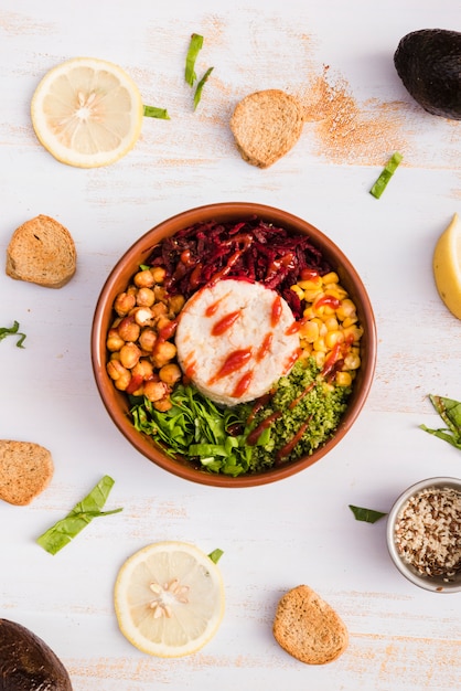 Bol avec du riz et des légumes entourés de citron et de pain sur un fond texturé blanc