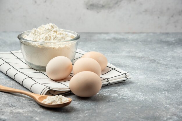 Bol de farine et oeufs crus sur nappe.