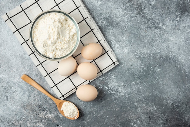 Bol de farine et oeufs crus sur nappe.