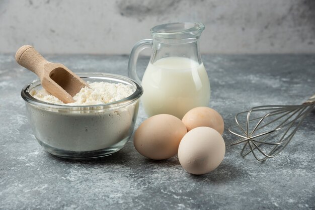 Bol de farine, œufs et ustensiles de cuisine sur table en marbre.