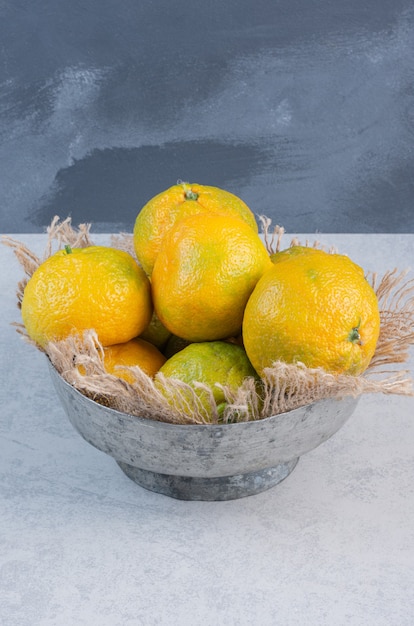 Bol en fer plein de mandarines (oranges, clémentines, agrumes) sur fond gris.