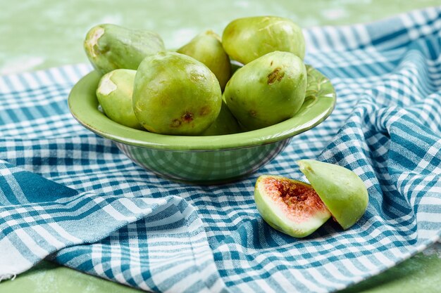 Un bol de figues vertes juteuses et une tranche de figues sur nappe bleue.