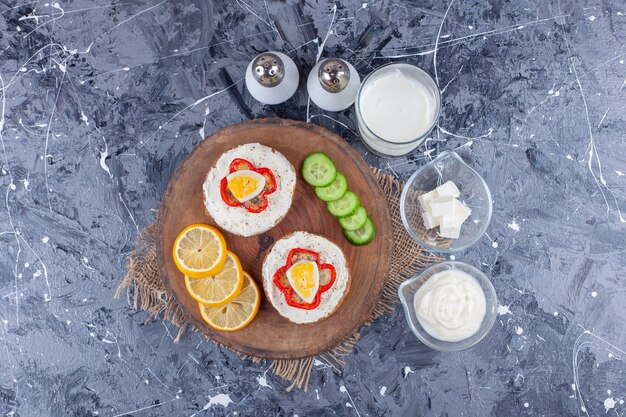 Un bol de fromage, un verre de thé à côté de pain au fromage, des tranches de citron et de concombre sur une planche, sur la table bleue.