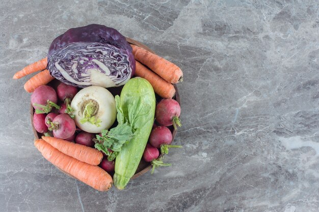 Bol garni de carottes, courges, navets, chou rouge et feuilles de navet sur marbre.