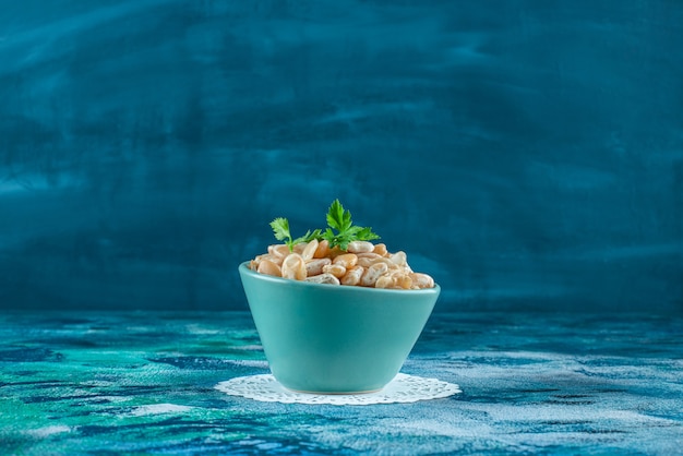 Un bol de haricots blancs avec du persil, sur le fond bleu.