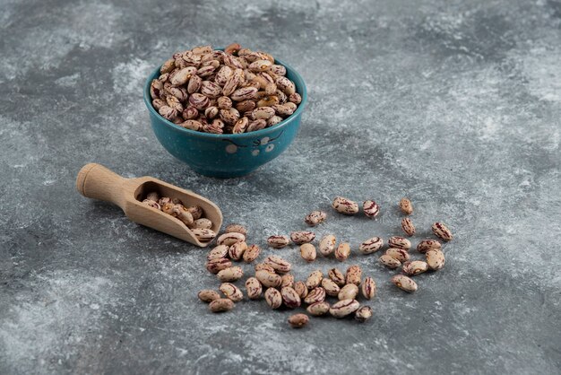 Bol de haricots secs et cuillère en bois sur marbre.