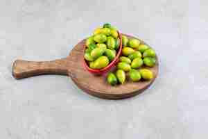 Photo gratuite bol de kumquats à côté d'un tas sur une planche de bois en surface de marbre.