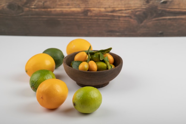 Photo gratuite bol de kumquats frais, citrons verts et citrons sur blanc.