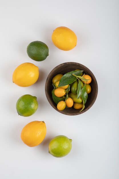 Bol de kumquats frais, limes et citrons sur fond blanc.