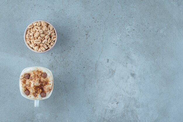 Un bol de muesli et une tasse de cappuccino, sur fond bleu.