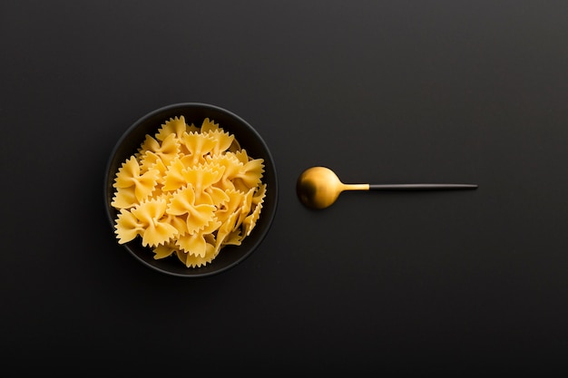 Bol noir avec des pâtes et une cuillère sur une table sombre