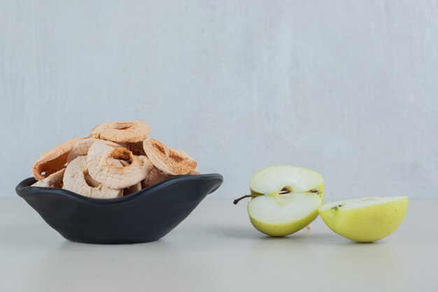 Un bol noir plein de pommes séchées avec des tranches de pomme fraîche.