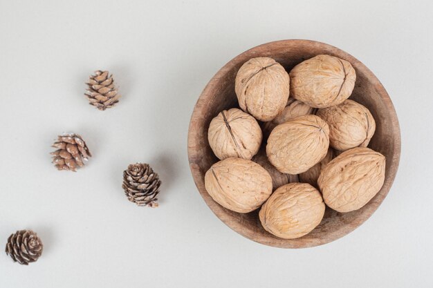 Bol de noix et de pommes de pin sur une surface beige