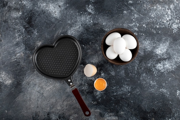 Photo gratuite bol d'oeufs blancs et de jaune à côté de la casserole en forme de coeur.