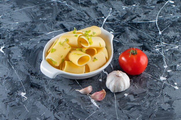 Bol de pâtes de calamarata bouillies avec des légumes sur une surface en marbre.