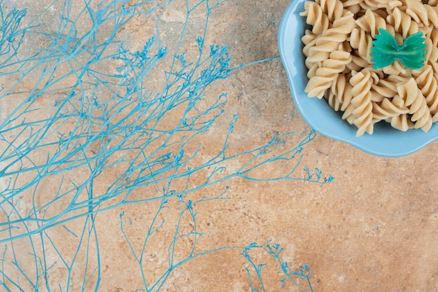 Photo gratuite bol de pâtes fusilli avec plante bleue sur fond orange