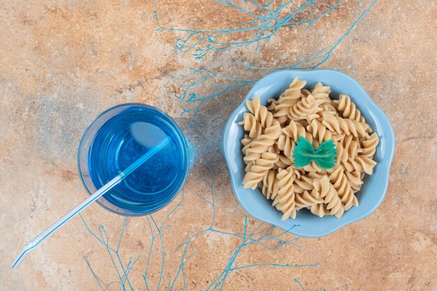 Bol de pâtes fusilli et verre de cocktail bleu sur un espace en marbre.