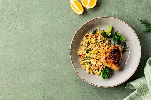 Bol avec des pâtes de poulet orzo avec des légumes de style méditerranéen sur un fond vert