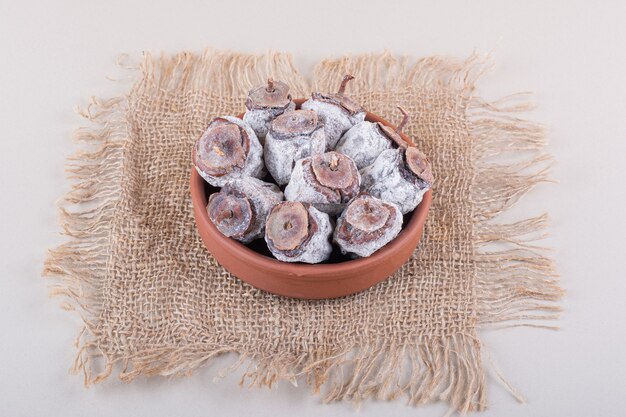 Bol plein de kakis séchés et de toile de jute sur fond blanc. photo de haute qualité