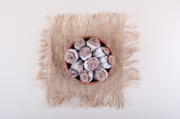 Bol plein de kakis séchés et de toile de jute sur fond blanc. photo de haute qualité