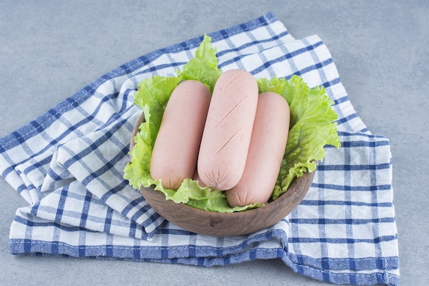 Un bol plein de saucisses et de feuilles de laitue.