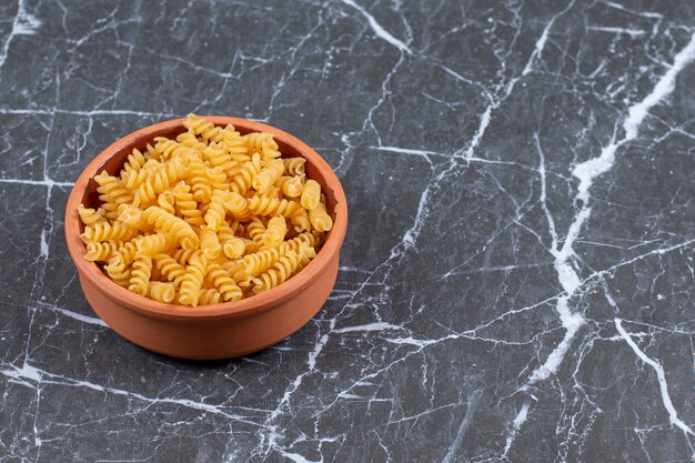 Bol en poterie plein de pâtes crues en spirale.