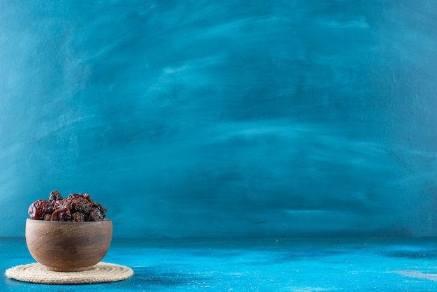 Un bol de prunes séchées sur un dessous de plat , sur la table bleue.