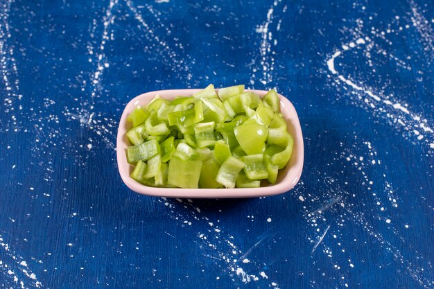 Bol rose de poivrons verts tranchés sur une surface en marbre