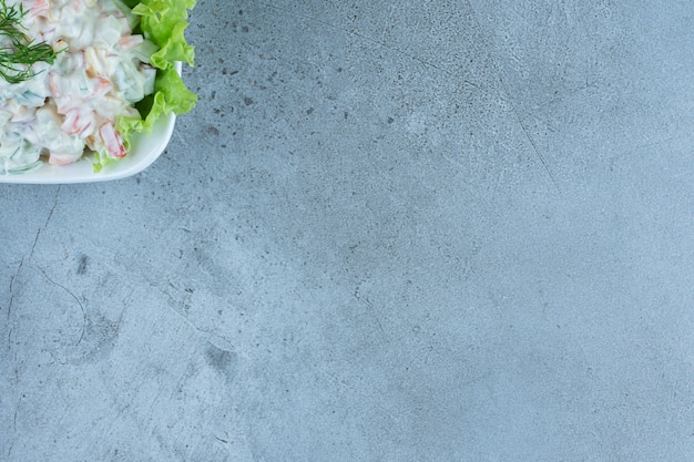 Bol de salade d'olivier avec une feuille de laitue sur marbre.