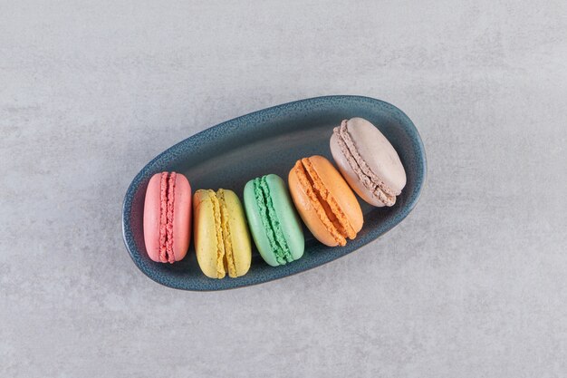 Bol sombre de macarons sucrés colorés sur table en pierre.