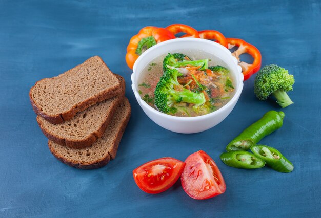 Bol de soupe au poulet, légumes et pain sur la surface bleue